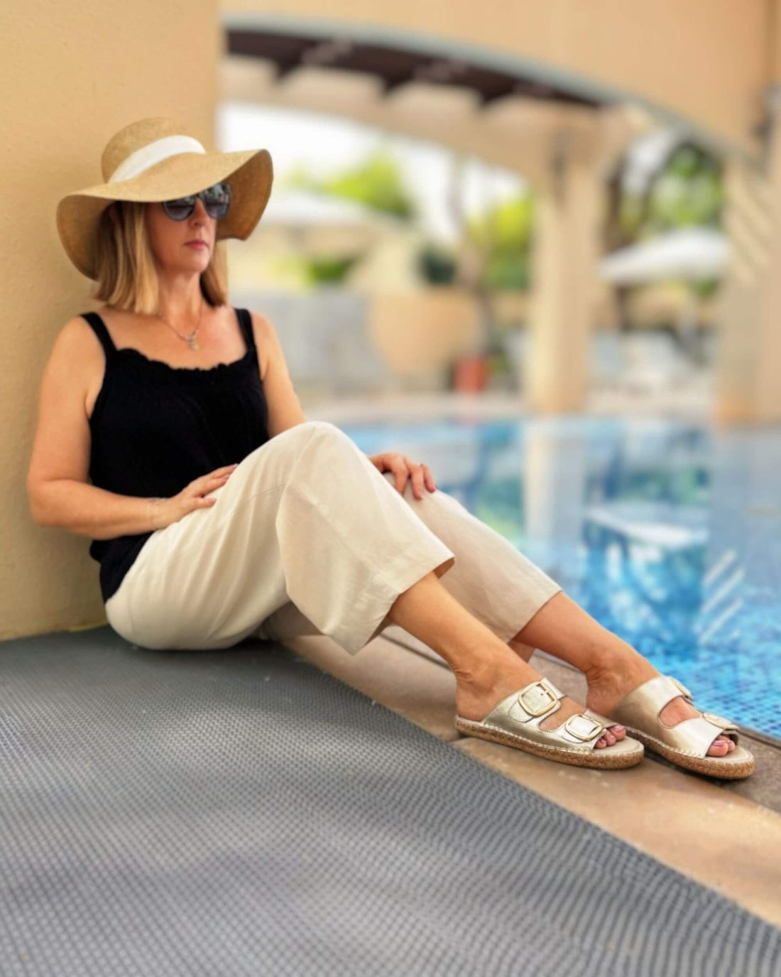 Urban Espadrille Slide in Champagne — close-up on feet, champagne gold metallic leather slides with gold double buckles, worn with cream trousers | Shoeq